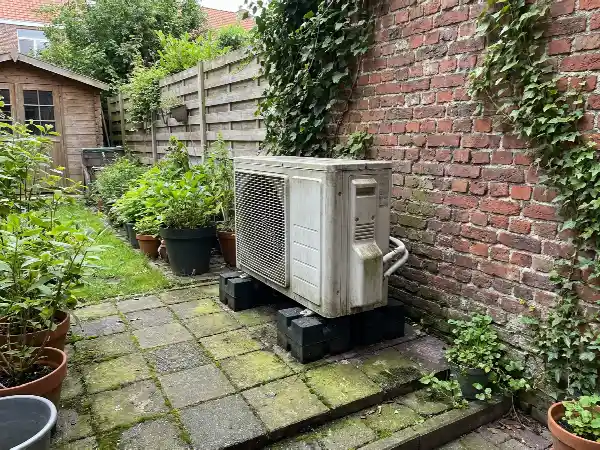 Groupe extérieur de climatisation posé au sol dans un jardin